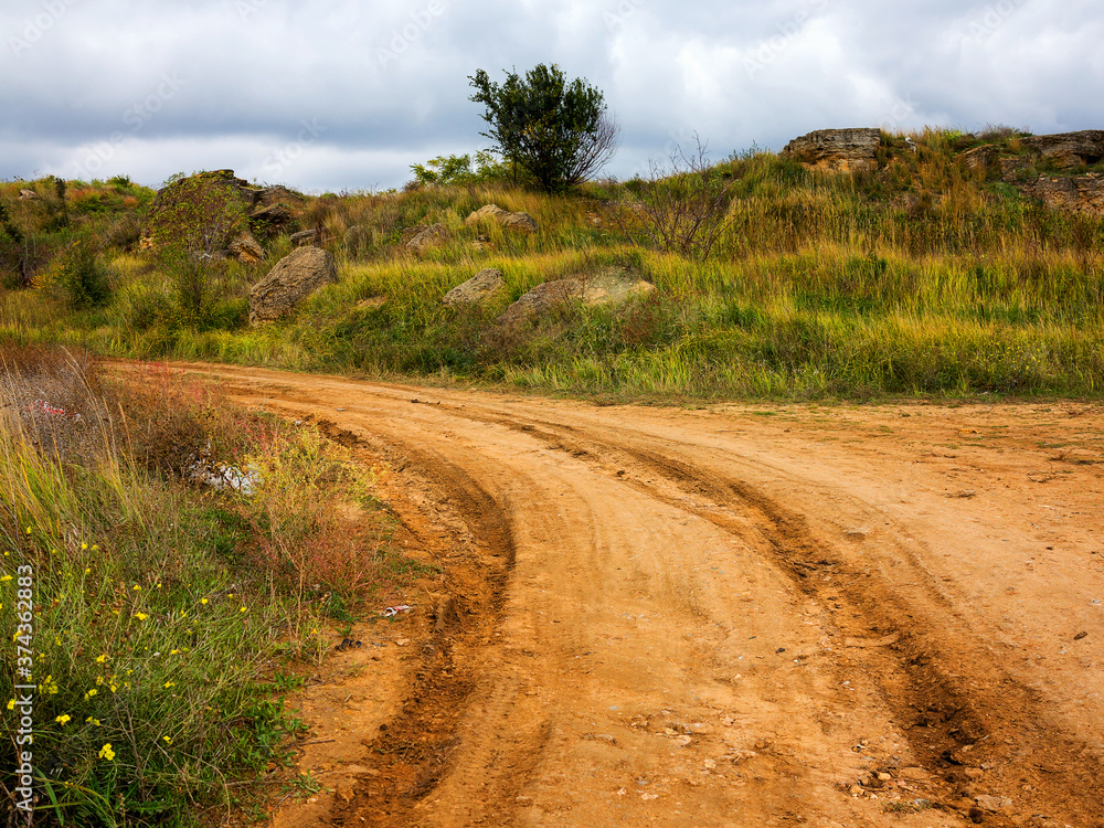 Dirt road with puddles and mud, washed out after a rain on a cloudy autumn day. Authentic rural landscape. Traces of off-road tires. Bad road. Dirt road with puddles and mud, washed out after a rain on a cloudy autumn day. Authentic rural landscape. Traces of off-road tires. Bad road.