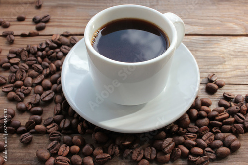 Cup of coffee with beans. Black coffee and scattered coffee beans on wooden table