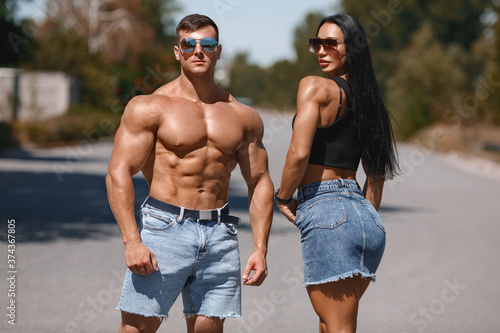 Muscular couple outdoors. Sporty man and woman showing muscles