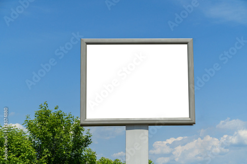 Billboard with white space for layouts and posters among the trees against the blue sky and trees.