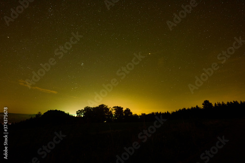 Yellowish night sky with many stars and constellations, the planet Mars can be seen, the forest is shown in silhouette. Germany, Baden-Wuerttemberg.