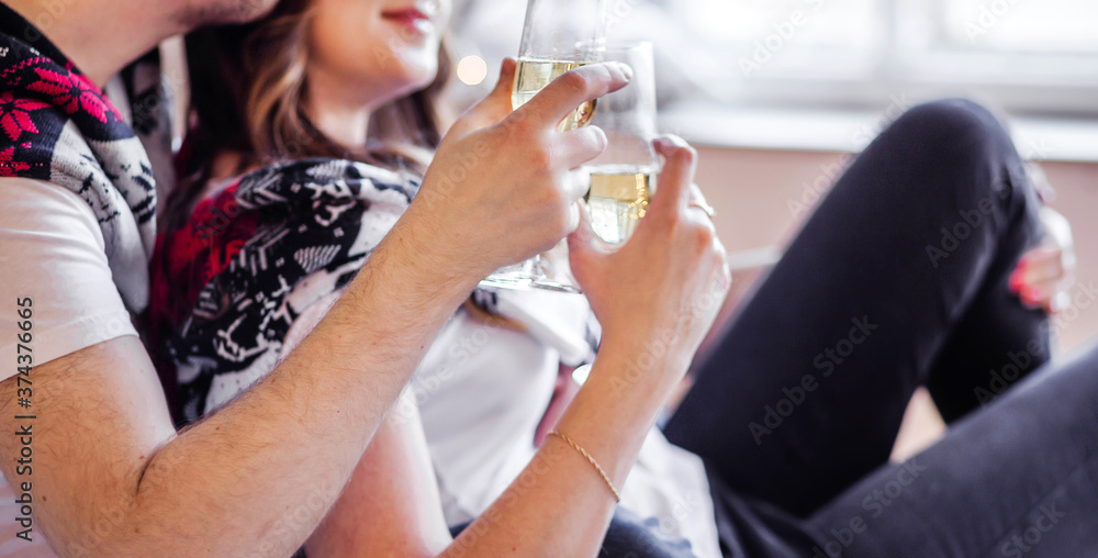 Fototapeta premium Man and woman in white t-shirts and knitted sweaters hold glasses of champagne in their hands