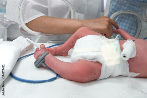 Nurse takes action to monitor and care for premature baby  selective focus - baby foot and nurse arm. Newborn is placed in the incubator. Neonatal intensive care unit