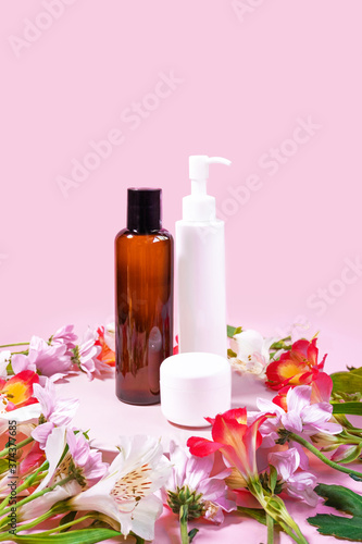 Set of cosmetic products on pink background decorated with flowers. Presentation poster. Banner with text. Space for text. Mock up of cosmetic product. Dispenser bottle, jar of cream,dark glass bottle