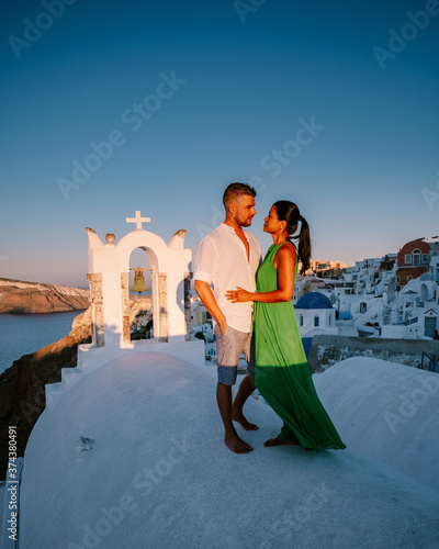 Santorini Greece, young couple on luxury vacation at the Island of Santorini watching sunrise by the blue dome church and whitewashed village of Oia Santorini Greece during sunrise during summer photo