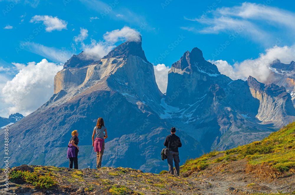 A group of three tourists looking upon the Andes peaks of Cuernos del Paine in Chilean Patagonia. Unsharp foreground, sharp background.