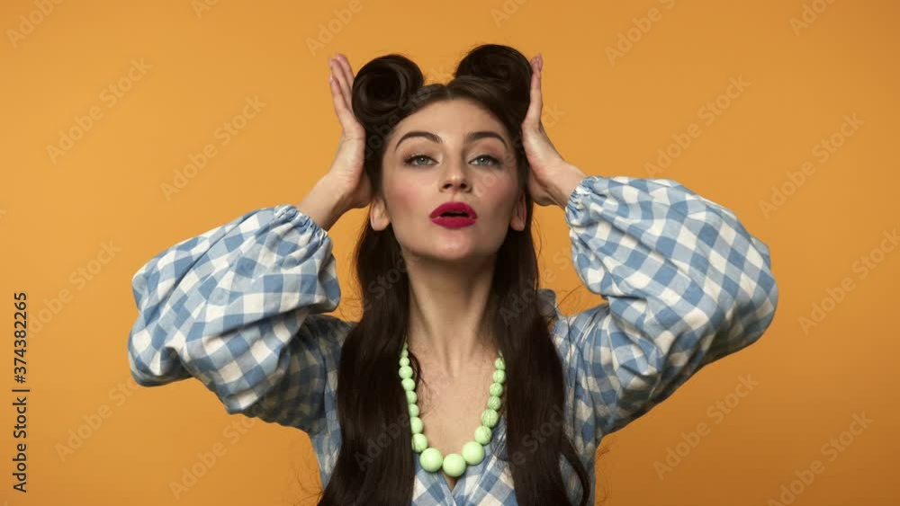 Elegant pin up woman checking hairstyle and winking with gently smile Elegant pin up woman checking hairstyle and winking with gently smile