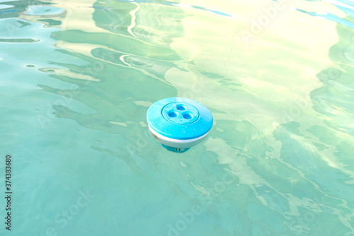 Blue chlorine dispenser floating in a home pool, cleaning and care of the domestic pool.