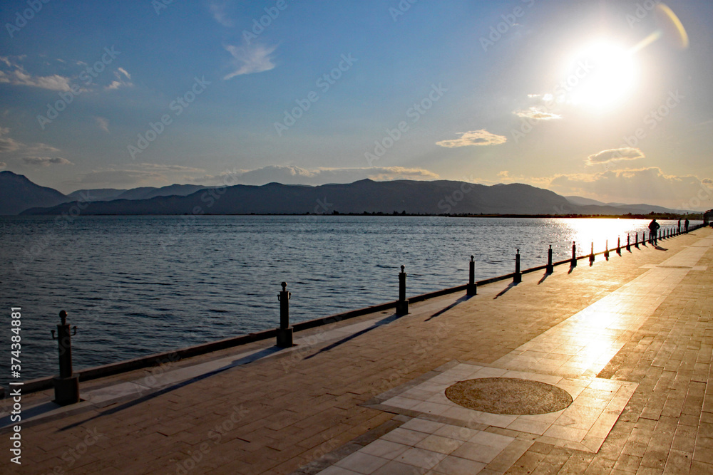 Obraz premium Photo taken into the evening sun as it sinks slowly in the west, casting shadows from the railings on to an ornamental walkway in a Turkish seaside resort.