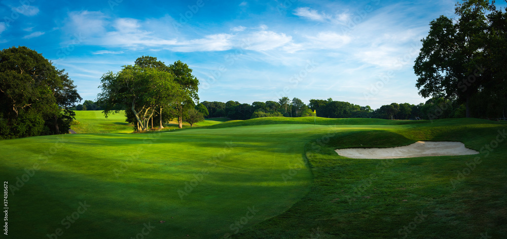 Panoramic landscape over the lush green fairway, the green, and the sand bunker at sundown Panoramic landscape over the lush green fairway, the green, and the sand bunker at sundown