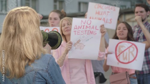 Back view of young Caucasian woman shouting through megaphone with blurred people supporting demonstration against animal rights violation at the background. Protest leader encouraging eco-activists.