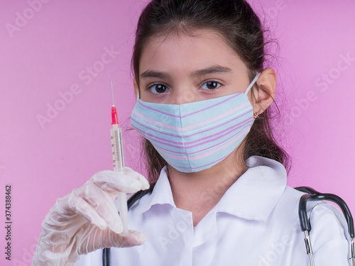 Little funny girl with a collorful stethoscope while wearing Doctor's uniform.  colorful mask.  syringe, covid 19. vaccination photo