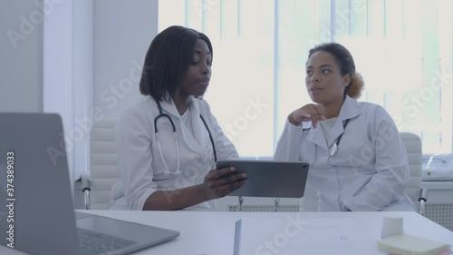 African physician showing medical application on tablet to colleague, consilium photo