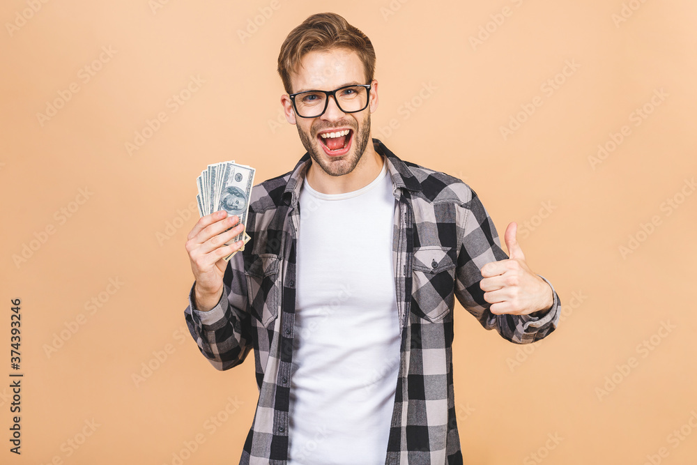 Happy winner! Young surprised rich man in casual holding money dollar bills isolated over beige background. Happy winner! Young surprised rich man in casual holding money dollar bills isolated over beige background.