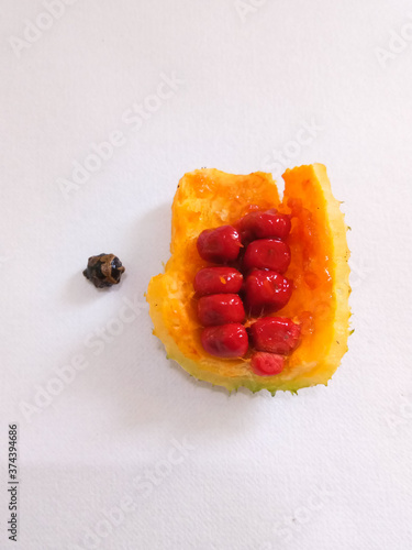 fresh ripened fruits of spine gourd is opened to show the red juicy sweet fruit-lets and unique shaped seeds with brown shades along with its stem and leaves in white background isolated  photo