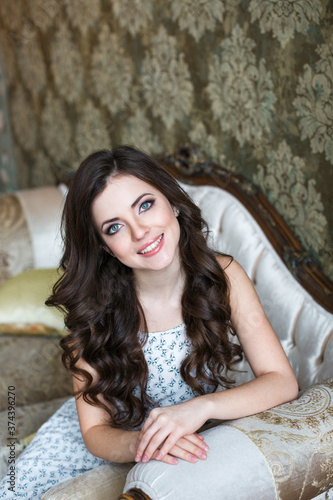 Beautiful young smiling woman with curly hair on a vintage sofa. © BestForYou