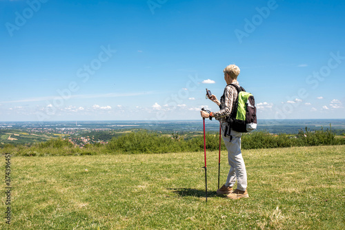 Active senior woman hiker taking a break in the nature while checking coordinates with hand held GPS navigator device