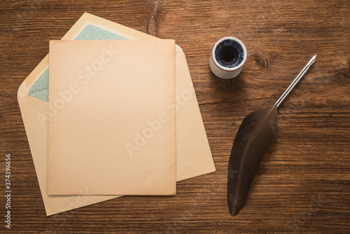 Envelope, goose feather, inkwell on a wood table  	
