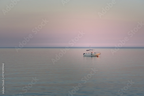 In the evening at sunset a small white boat in Italy is on the calm sea and small waves