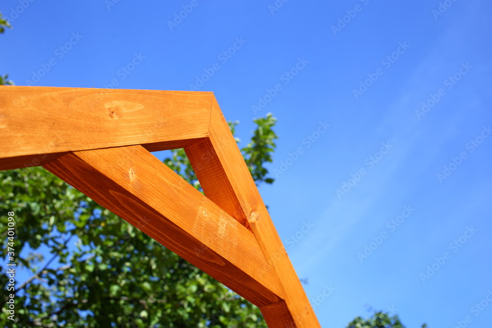 Large letter A made of wooden blocks painted with brown orange protective impregnation. Part of rafters of roof of orphanage, gazebo against blue sky and green leaves of tree on sunny summer day Large letter A made of wooden blocks painted with brown orange protective impregnation. Part of rafters of roof of orphanage, gazebo against blue sky and green leaves of tree on sunny summer day