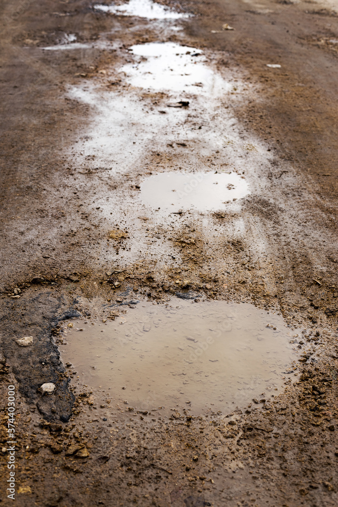 Bad road. Pits, potholes and puddles after rain on paved road. Background is an old road with cracked asphalt, gravel and sand Bad road. Pits, potholes and puddles after rain on paved road. Background is an old road with cracked asphalt, gravel and sand