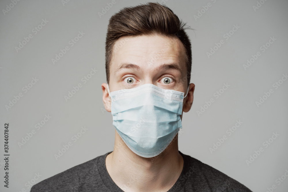 portrait of a young man of Caucasian appearance in a blue mask looks at the camera. grey t-shirt, grey background. a protective agent against the pandemic face. emotion surprise portrait of a young man of Caucasian appearance in a blue mask looks at the camera. grey t-shirt, grey background. a protective agent against the pandemic face. emotion surprise