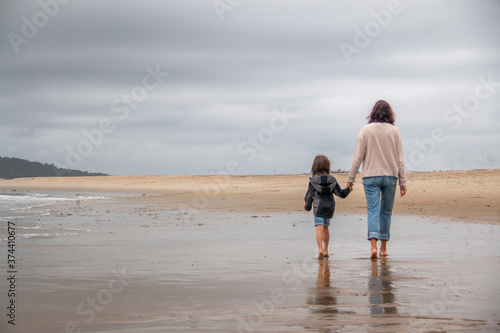 Mother and daughter walking down a wooden path to the beach