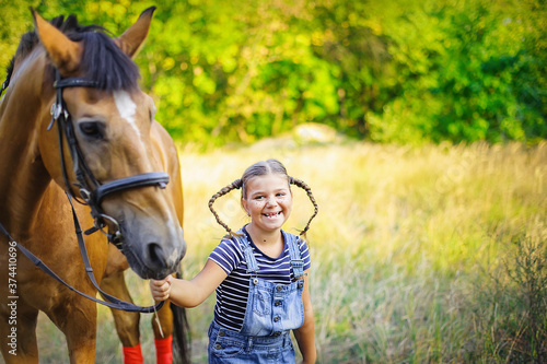 Laughing girl leads to bridle of horse. Red horse on background of autumn yellow trees. World Smile Day