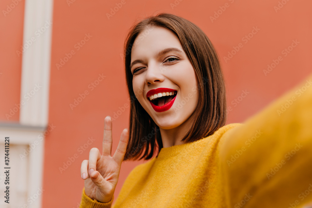 Cute female model with short straight hair posing on pastel background. Enthusiastic young woman in yellow outfit making selfie. Cute female model with short straight hair posing on pastel background. Enthusiastic young woman in yellow outfit making selfie.