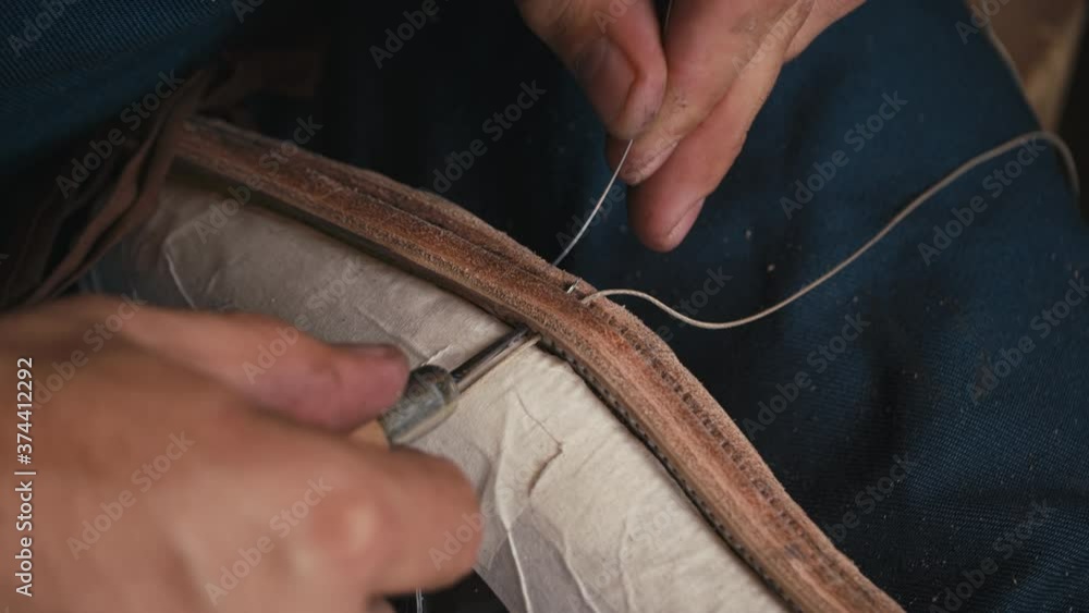 Close up shoemaker's hands stitching shoe with awl and thread. Workshop hipsters. Craft production. Cinematic light