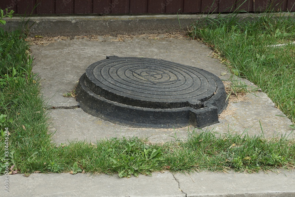 one black iron manhole on gray concrete in green grass outside