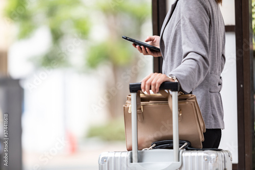 バス停でスーツケースを持ってバスを待つ女性　