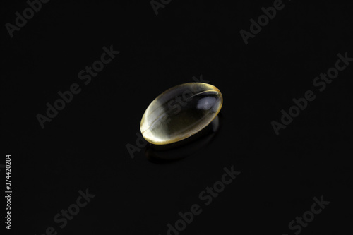 single gel tab pill or supplement isolated on a black background with reflection, vitamin E or vitamin D fish oil with copy space
