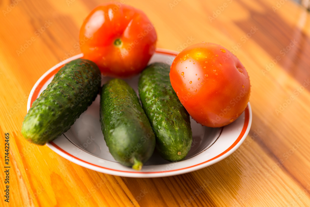 Fresh Tomatoes and Cucumbers on Plate Against Wooden Table. Fresh Tomatoes and Cucumbers on Plate Against Wooden Table.