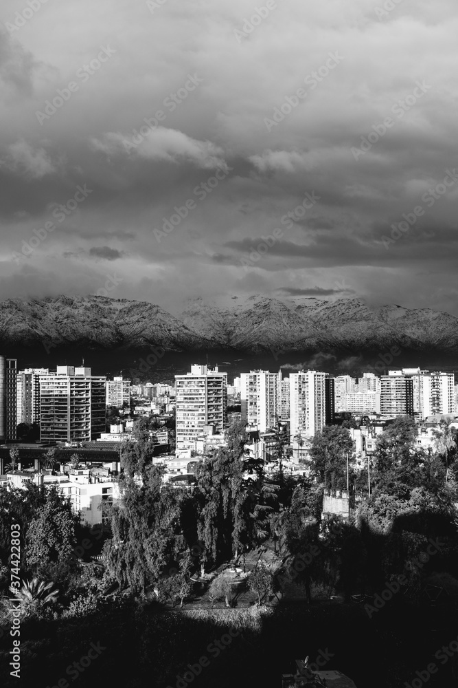 Amazing cloudy sky over Santiago skyline, Santa Lucía hill and the snowed The Andes Mountains, and a beautiful sunlight over the city, Chile (in black and white)
