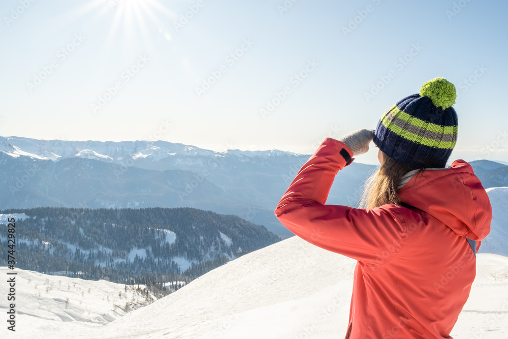 Portrait of a woman in a winter hat with a pom-pom on a background of a winter mountain landscape