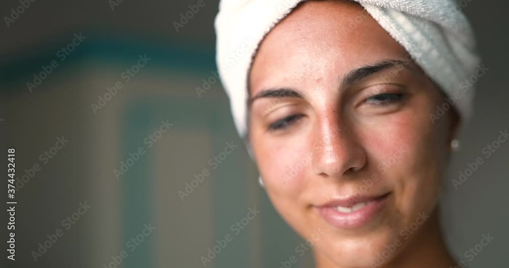 Close up of an young woman with towel on her head and face just cleaned from impurities is ready for day or night cream is smiling in camera in a bathroom. Close up of an young woman with towel on her head and face just cleaned from impurities is ready for day or night cream is smiling in camera in a bathroom.