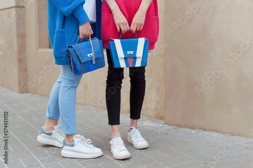 Two fahionable young women wearing knit cardigans and jeans. They are holding snake print bags in hands. Street style. Outdoor.  photo