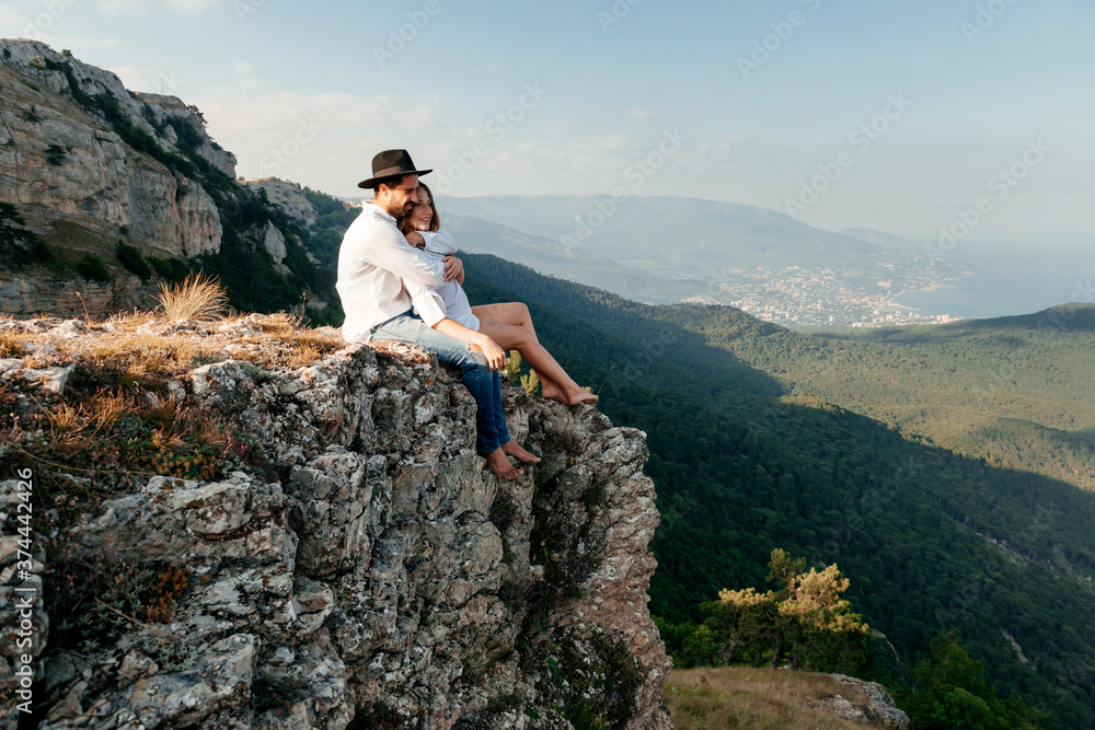 Attractive young loving couple of man in white shirt and blue jeans with girl in dress on sunny outdoor background in the green mountain landscape