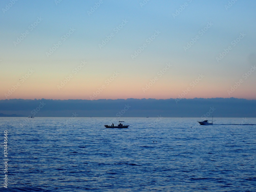 グラデーションの夜明けの空と穏やかな海に浮かぶ漁船