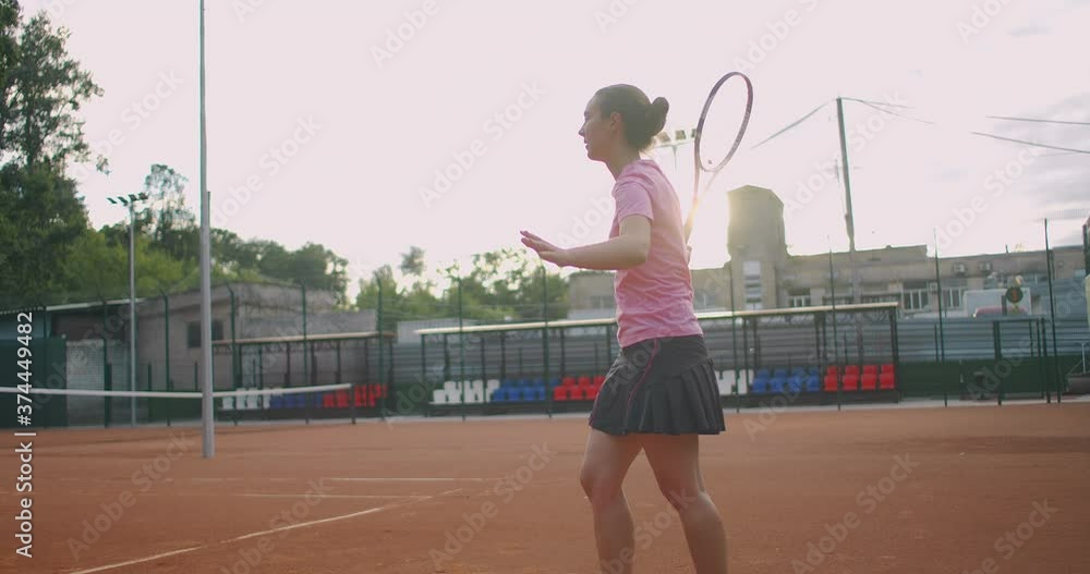 Side view of a young Caucasian woman playing tennis on a court, returning a ball in slow motion Side view of a young Caucasian woman playing tennis on a court, returning a ball in slow motion