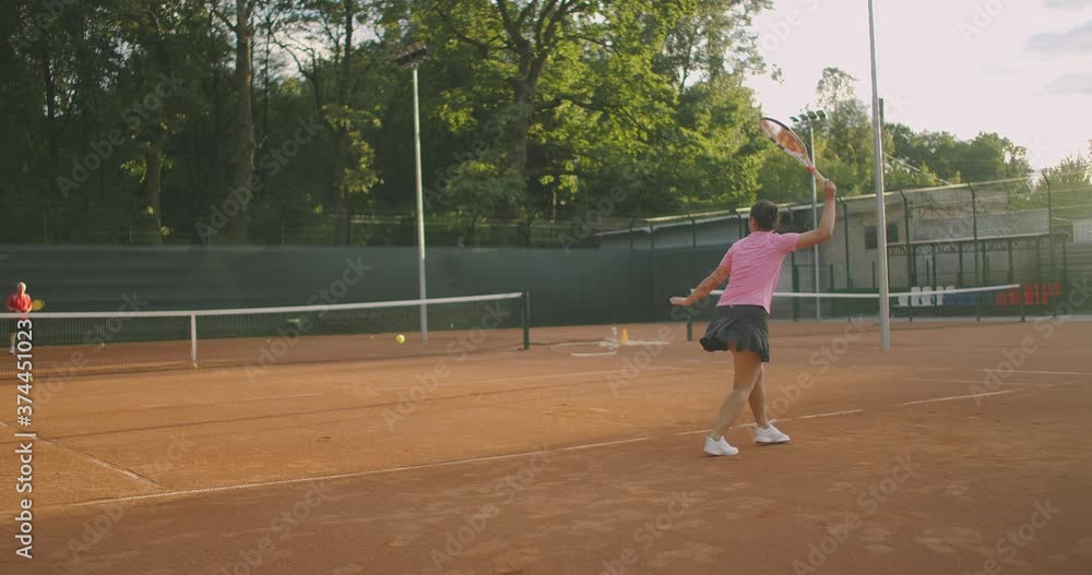 Young woman walking through tennis court with racket. Backside view of attractive brunette female in blue shirt and black shorts entering tennis hardcourt. Full length follow shot with copy space Young woman walking through tennis court with racket. Backside view of attractive brunette female in blue shirt and black shorts entering tennis hardcourt. Full length follow shot with copy space