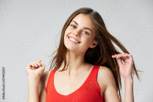 beautiful woman in a red t-shirt touches hair with her hands on a light background 