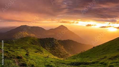 Fabulous sunrise in the mountains. The pink light of the sun illuminates the green hills covered with a gentle veil of fog