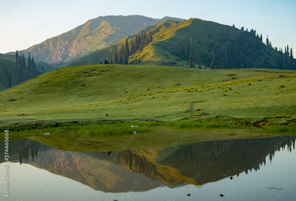 Fototapeta premium lush green landscape with small lake and mountains - mountain reflection on the water - siri paye Medows clear sky