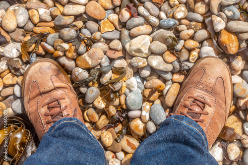 A pair of male feet in brown leather does on a pebble beach. photo