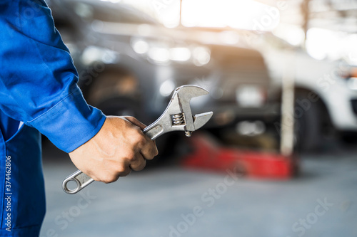 Mechanic close up fixing repairing car engine automobile vehicle parts examining screwing using tools wrench equipment working hard in workshop garage support and service in overall work uniform