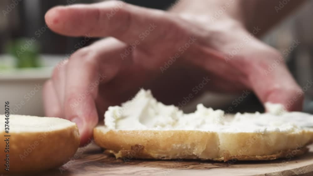 Man hands spreading cream cheese on bagel on wood board Man hands spreading cream cheese on bagel on wood board
