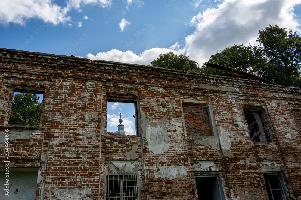 Fototapeta premium ruins of an old manor house among green trees against a blue sky
