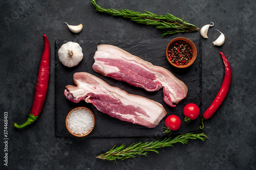 raw pork breast with spices on a slate board on a stone background